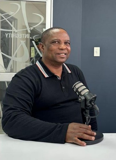 Portrait of Peter Mehlape smiling at the studio table beside a podcast microphone
